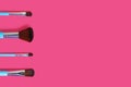 A set of four makeup brushes on a pink background