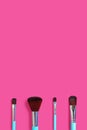 A set of four makeup brushes on a pink vertical background