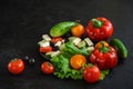 Set of fresh ripe whole and chopped vegetables for cooking Greek salad on a black concrete surface with space for text, Royalty Free Stock Photo