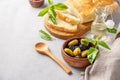 A set of green and black dried olives in bowl with fresh ciabatta bread on a light background with olive oil and basil. The Royalty Free Stock Photo