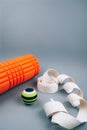 Set of green fascia release ball, orange bumpy foam massage roller for trigger points and belt over grey background.