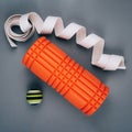 Set of green fascia release ball, orange bumpy foam massage roller for trigger points and belt over grey background.