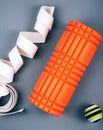 Set of green fascia release ball, orange bumpy foam massage roller for trigger points and belt over grey background.