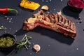 Set of grilled sliced T-bone steak with grilled corn, sauce, chilli, rosemary, salt, garlic on black background