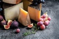 Set of hard cheeses with grapes and figs on dark table. traditional pieces of Spanish, French, Italy cheese