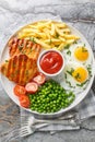 Set lunch Grilled steak with green peas, fried egg, french fries, tomatoes and sauce close-up in a plate. Vertical top view Royalty Free Stock Photo