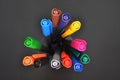 Set of multi-colored bright pens standing in a transparent glass, top view on black background, closeup