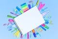 A set of multi-colored school and office stationery laid out under a blank sheet of notebook.