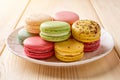 Set of multicolored macaroons on a white plate over wooden table. Colorful macaron cakes variety. Delicious french dessert. Sweets