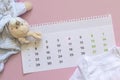 Set of newborn accessories in anticipation of child - calendar with circled number 4 four baby clothes, toys on pink background