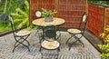 Set of outdoor dining furniture. Mosaic tile and iron chairs and table on a grey brick patio in a lush garden. Cozy Royalty Free Stock Photo