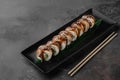 Set of philadelphia rolls with eel, smoked salmon, avocado and green bamboo leaf in a black ceramic plate with chopstick on a dark Royalty Free Stock Photo