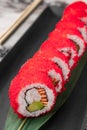 Set of philadelphia rolls with red flying fish caviar, avocado, salmon and green bamboo leaf in a black ceramic plate with Royalty Free Stock Photo