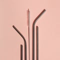 A set of reusable cocktail tubes and cleaning brushes on a pink background. The concept of reducing waste.