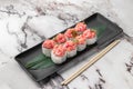 Set of rolls with salmon, red flying fish caviar and green bamboo leaf in a black ceramic plate with chopstick on a bright Royalty Free Stock Photo