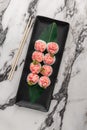 Set of rolls with salmon, red flying fish caviar and green bamboo leaf in a black ceramic plate with chopstick on a bright Royalty Free Stock Photo