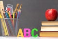 A set of school supplies. A stack of textbooks, an apple, letters of the alphabet A, B, C, pencils, brushes, paints.