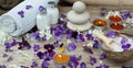 Set for spa treatments with bath salt, stones for hot massage and skin lotions in the midst of small purple flowers of pansies Royalty Free Stock Photo