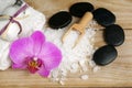 Set for spa treatments with lotions for skin, orchid flowers, bath salt and black stones for a hot massage on a wooden background Royalty Free Stock Photo