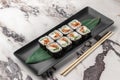Set of square maki rolls with fried salmon, curd cheese and green bamboo leaf in a black ceramic plate with chopstick on a bright Royalty Free Stock Photo