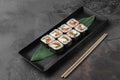 Set of square maki rolls with fried salmon, curd cheese and green bamboo leaf in a black ceramic plate with chopstick on a dark Royalty Free Stock Photo