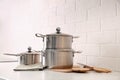 Set of stainless steel cookware and kitchen utensils on table near white brick wall Royalty Free Stock Photo