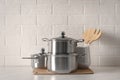 Set of stainless steel cookware and kitchen utensils on table near white brick wall Royalty Free Stock Photo