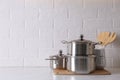 Set of stainless steel cookware and kitchen utensils on table near white brick wall, space for text Royalty Free Stock Photo