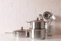 Set of stainless steel cookware and kitchen utensils on table near white brick wall, space for text Royalty Free Stock Photo