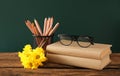 Set of stationery, glasses and flowers on wooden table near chalkboard. Teacher`s Day