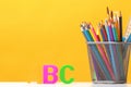 Set of stationery. Pencils, brushes, paints, letters of the alphabet A, B, C on the background of the yellow wall.