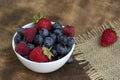 Set of summer berries in a small white bowl on a napkin and wooden background. Blueberries, raspberries, and strawberries are a Royalty Free Stock Photo