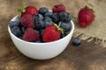 Set of summer berries in a small white bowl on a napkin and wooden background. Blueberries, raspberries, and strawberries are a Royalty Free Stock Photo