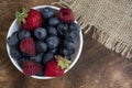 Set of summer berries in a small white bowl on a napkin and wooden background. Blueberries, raspberries, and strawberries are a Royalty Free Stock Photo