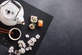 Set of sushi and maki rolls with branch of white flowers and teapot with the inscription green tea on stone table