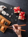 Set of sushi and maki rolls, hand with chopsticks, gift boxes and branch of white flowers on stone table. Royalty Free Stock Photo