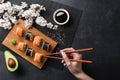 Set of sushi and maki rolls, sliced avocado, hand with chopsticks and branch of white flowers on stone table Royalty Free Stock Photo