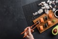 Set of sushi and maki rolls with sliced avocado, hand with chopsticks and branch of white flowers on stone table Royalty Free Stock Photo