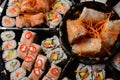 Set of sushi rolls on a black plastic platter decorated with soy sauce and spices.