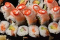 Set of sushi rolls on a black plastic platter decorated with soy sauce and spices.