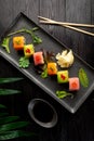 Set of sushi rolls on a black plate on a black wooden background with green leaves of a houseplant Royalty Free Stock Photo