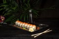 Set of sushi rolls on a black plate on a black wooden background with green leaves of a houseplant Royalty Free Stock Photo