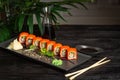 set of sushi rolls on a black plate on a black wooden background with green leaves of a houseplant Royalty Free Stock Photo