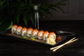 set of sushi rolls on a black plate on a black wooden background with green leaves of a houseplant Royalty Free Stock Photo