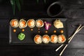 set of sushi rolls on a black plate on a black wooden background with green leaves of a houseplant Royalty Free Stock Photo