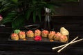 Set of sushi rolls on a black plate on a black wooden background with green leaves of a houseplant Royalty Free Stock Photo