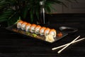 Set of sushi rolls on a black plate on a black wooden background with green leaves of a houseplant Royalty Free Stock Photo