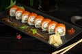 Set of sushi rolls on a black plate on a black wooden background with green leaves of a houseplant Royalty Free Stock Photo