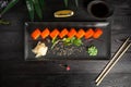 set of sushi rolls on a black plate on a black wooden background with green leaves of a houseplant Royalty Free Stock Photo