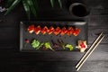 Set of sushi rolls on a black plate on a black wooden background with green leaves of a houseplant Royalty Free Stock Photo